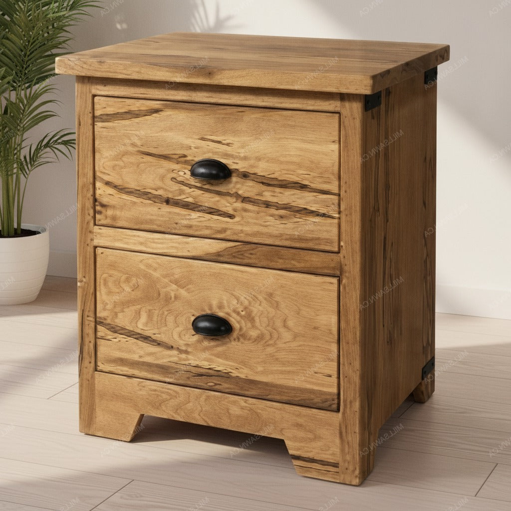 A rustic two-drawer wooden nightstand with a natural oak finish and black metal drawer pulls, shown in a brightly lit room next to a potted plant.