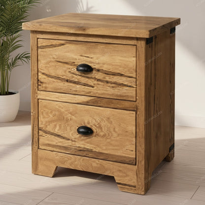 A rustic two-drawer wooden nightstand with a natural oak finish and black metal drawer pulls, shown in a brightly lit room next to a potted plant.
