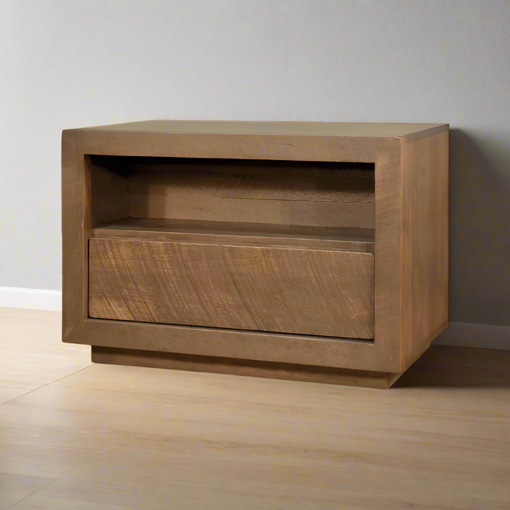 Wooden side table with a single drawer on a wooden floor against a gray wall.